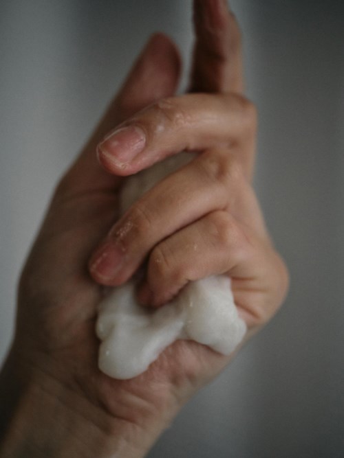 A hand squeezing a soft, white substance, possibly soap or foam, against a plain background.