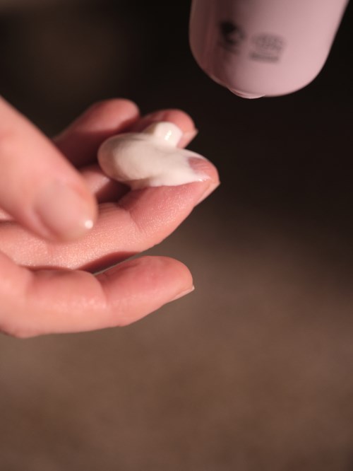 A hand applies lotion or cream from a bottle onto fingers in a close-up shot.