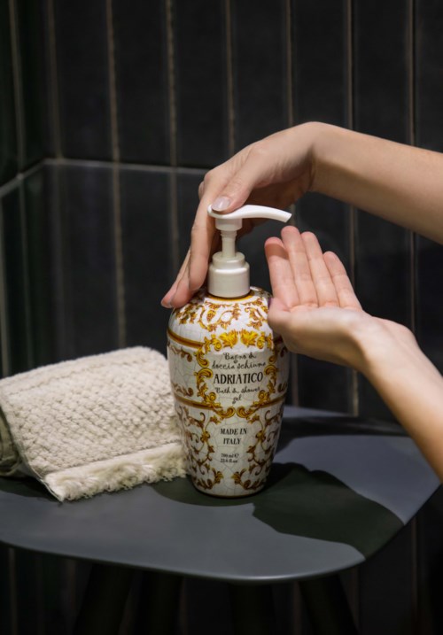 Hands using a soap dispenser on a dark wall, next to a folded cloth on a small table.