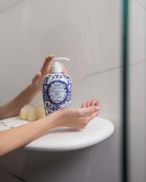 A person holds a blue and white ceramic pump bottle on a white table near a marble wall.