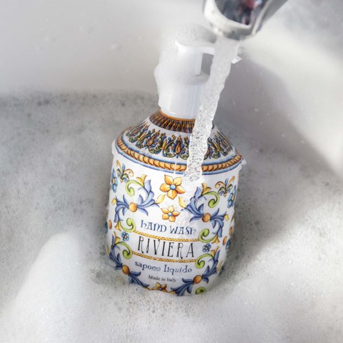 Koristeellinen käsisaippuapullo, jossa lukee 'Hand Wash Riviera', juoksevan veden alla pesualtaassa.