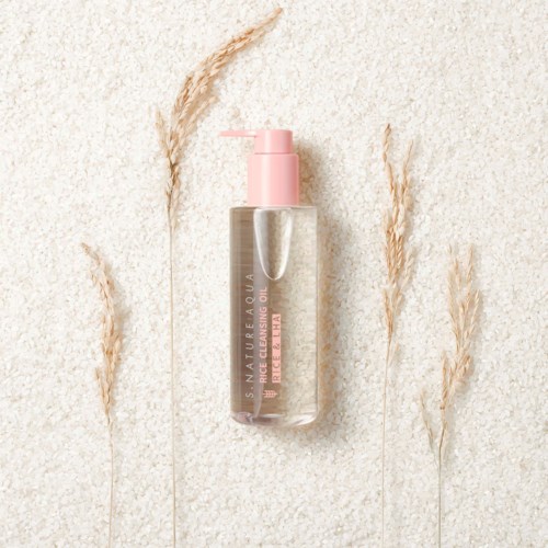 A clear bottle with a pink pump and label, surrounded by dried grass on a textured background.