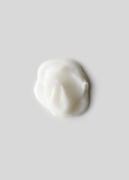 Een kleine hoop witte crème of lotion op een lichtgrijze achtergrond.