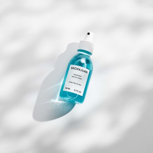 A blue spray bottle labeled 'SACHAJUAN' lying on a white surface with a shadow.