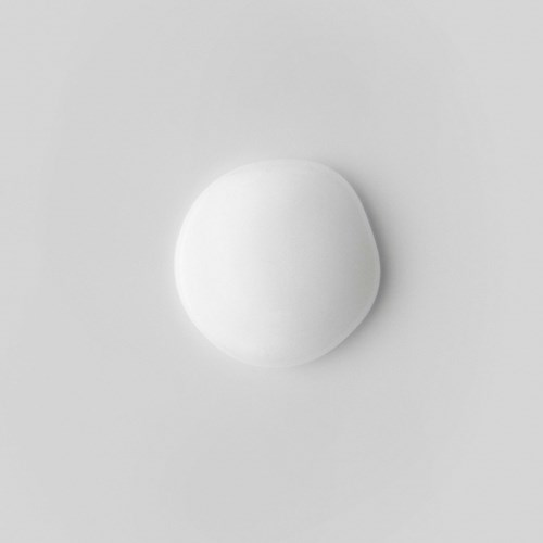 Ein weißer, runder Gegenstand auf hellgrauem Hintergrund, möglicherweise eine Pille oder ein kleiner Ball.