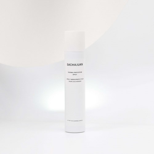 Een witte sprayfles met label 'SACHAUJAN' en beschrijving 'warmtebeschermende spray' voor haar op een eenvoudige achtergrond.