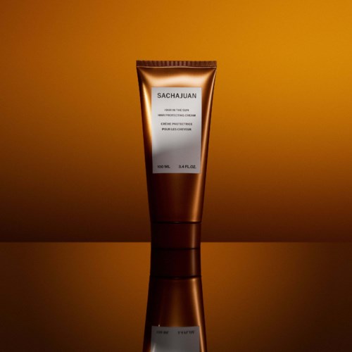 Ein braune Tube mit Gesichtcreme und weißem Etikett, auf einer spiegelnden Oberfläche gegen einen warmen Hintergrund.