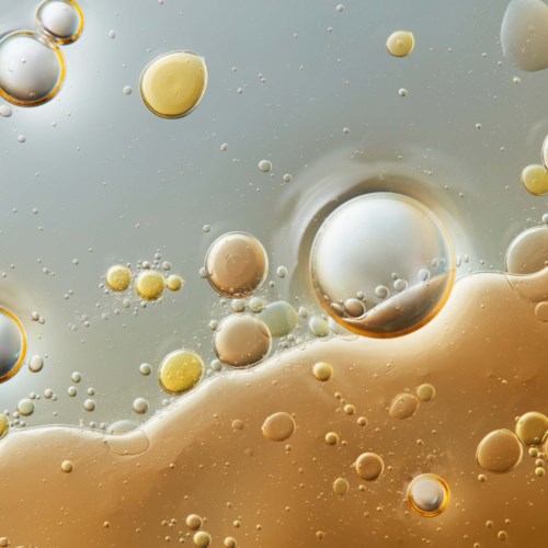 Öl und Wasser vermischen sich, bilden verschieden große Blasen vor buntem Hintergrund.