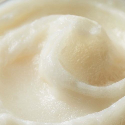 Nahaufnahme einer weißen, cremigen Substanz in einer Spiralform, wahrscheinlich Butter oder Sahne. Glatte und weiche Textur. Keine weiteren Elemente.