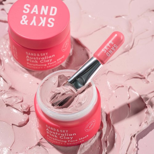 Pinkrote Dose mit australischer rosa Tonerde-Maske und Spatel, umgeben von rosa Ton auf rosa Hintergrund.