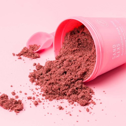 Pinke Behälter umgekippt, rosafarbenes Pulver verstreut, mit einem pinken Löffel in der Nähe auf pinkem Hintergrund.