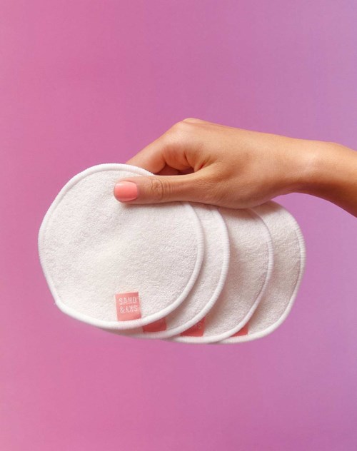 Eine Hand hält drei weiße Wattepads vor einem pinken Hintergrund.