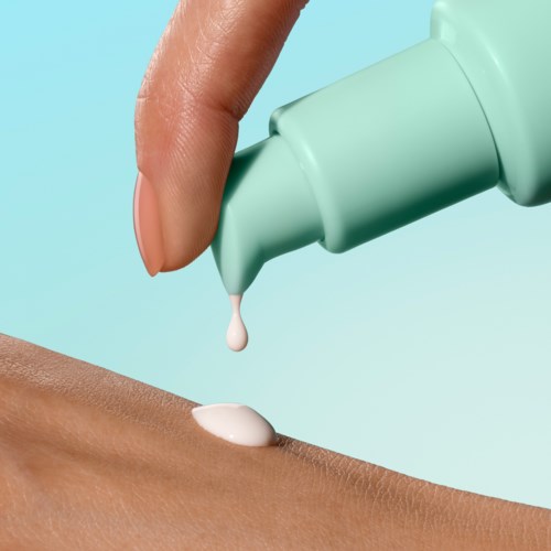 Eine Hand trägt Lotion oder Creme mit einer Tube auf die Haut auf, vor hellblauem Hintergrund.