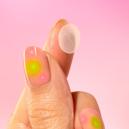 Zwei Finger mit Nagellack in Pink, Gelb und Grün sowie ein weißer runder Sticker oder Pad am Zeigefinger.