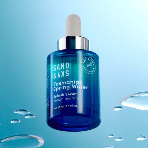 Eine blaue Flasche mit Sand & Sky Tasmanian Spring Water Splash Serum und Tropfer, schwebend im Wasser.
