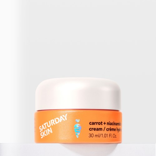 Een kleine oranje pot met witte dop met Saturday Skin wortelcrème, tekst op pot met een kleine wortel-icoon.