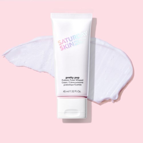 Een witte tube huidverzorgingscrème met roze en paarse tekst, op roze achtergrond met crème.