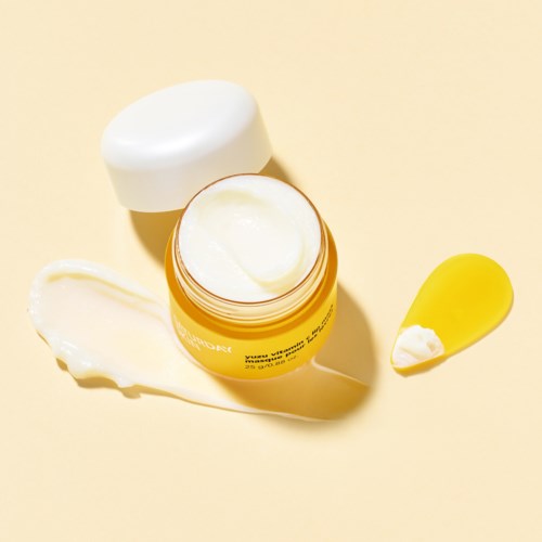 Een gele pot met crème erin, een beetje op een gele lepel, en wat crème op het oppervlak.