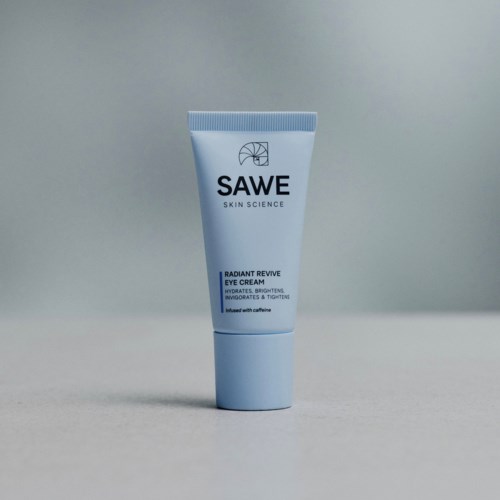 Eine hellblaue Tube mit SAWE Radiant Revive Eye Cream steht auf einer einfachen Oberfläche vor neutralem Hintergrund.