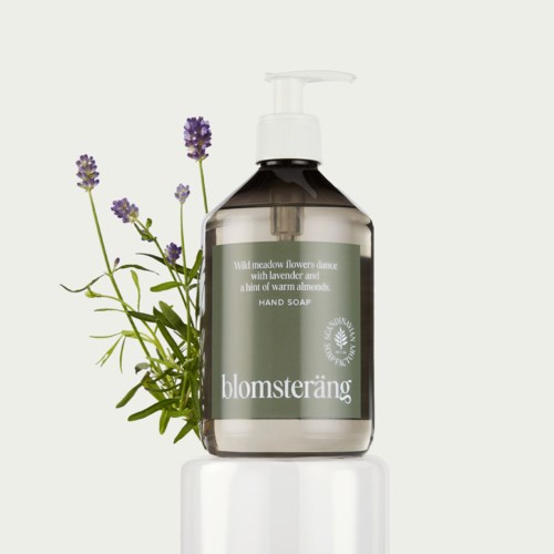 Eine klare Handseifenspenderflasche mit Lavendelpflanze daneben, beschriftet "blomsteräng."