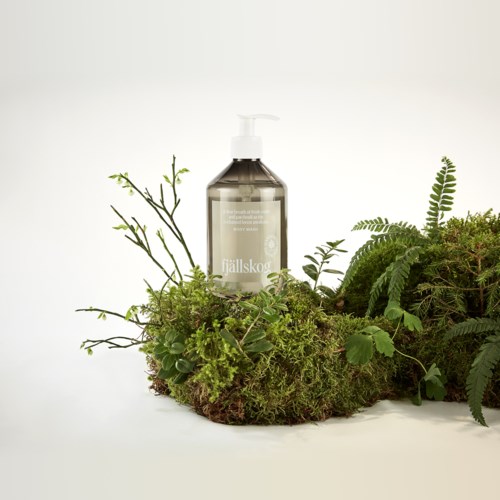 A clear soap bottle surrounded by green plants and moss, creating a natural, eco-friendly look.