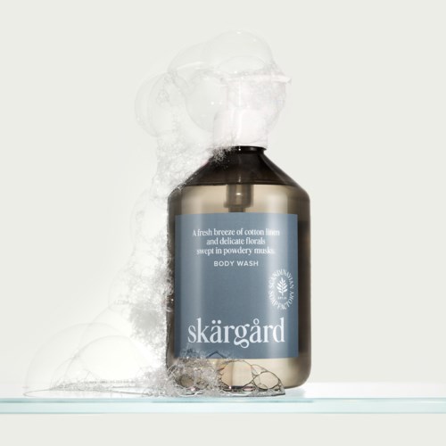 A dark bottle with light blue label, releasing foam and bubbles, labeled Skärgård body wash.