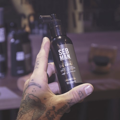 Eine Hand hält eine schwarze Flasche mit der Aufschrift "SEB MAN THE COOLER" in einem schwach beleuchteten Umfeld.
