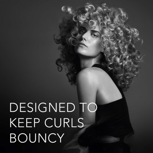 Svartvitt foto av en kvinna med stort, lockigt hår, iklädd en svart topp, tittar på kameran. Texten säger "Designed to keep curls bouncy."