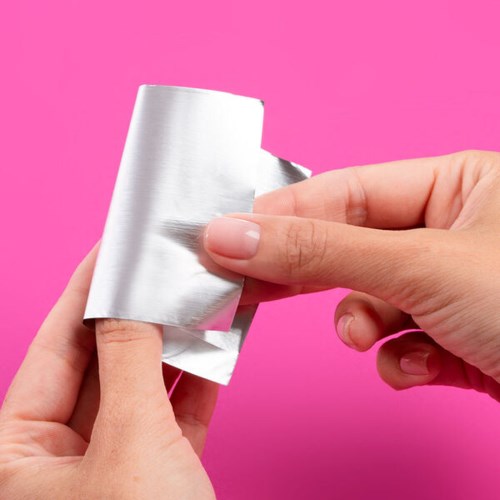 En person skalar av silverfolie från en rulle mot en rosa bakgrund.