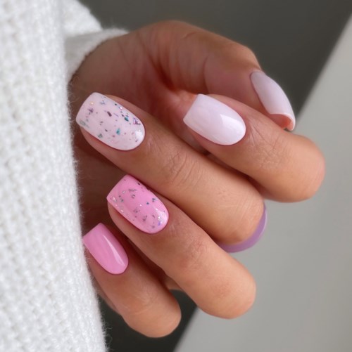 Eine Hand mit pinken und weißen Nägeln, einige Nägel haben Glitzer und Flecken, andere sind schlicht.