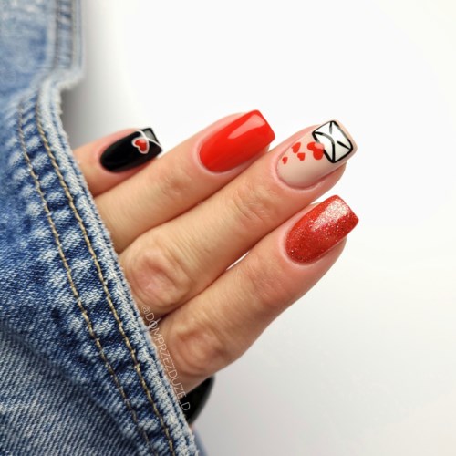 Nail art with red, black, and white colors, featuring hearts, an envelope, and glitter. Someone wears a denim jacket.