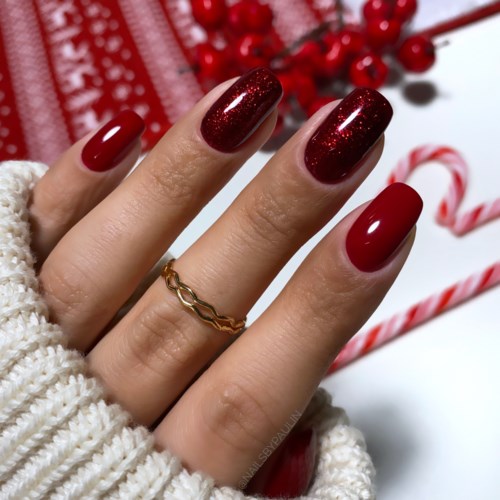 Die Hand hat rote und funkelnde Nägel, mit einem Goldring, und weihnachtliches Hintergrund mit Süßigkeiten und Beeren.