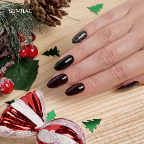 Eine Hand mit schwarzen und glitzernden Nägeln, Weihnachtsdekorationen, Tannenzapfen und festliche Ornamente auf einer Holzfläche.
