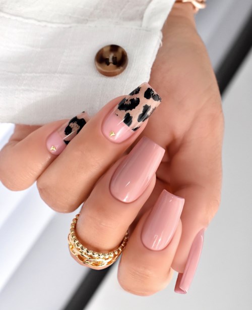 Nageldesign mit hellrosa Nagellack und Leopardenmuster, Goldringe an den Fingern, und Teil weißer Kleidung.
