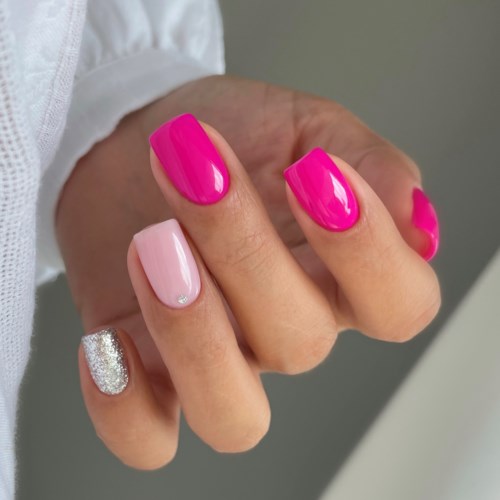 Eine Hand mit bunten lackierten Nägeln, pink und silberne Details, vor einfachem Hintergrund.