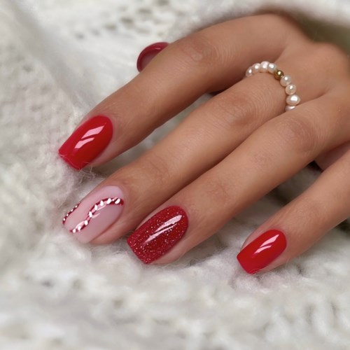 Rote und pinke Nägel mit festlichen Mustern und einem Perlenarmband am Finger.