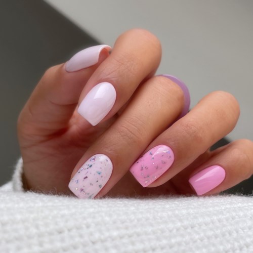  Handens naglar är rosa och vita med glitter och prickar, ett roligt nagellacksdesign.