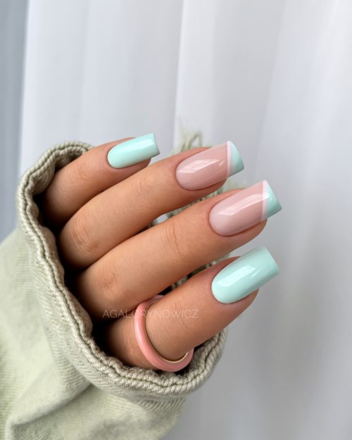 Eine Hand mit pastellblauen und rosa Nägeln trägt einen rosa Ring und einen gemütlichen Pullover.