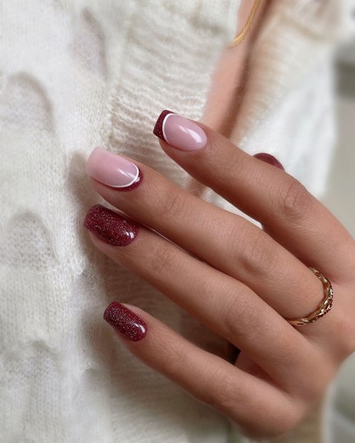 Manikürte Nägel mit rosa und rotem Glitterlack, ring am Finger, auf hellem Stoffhintergrund.