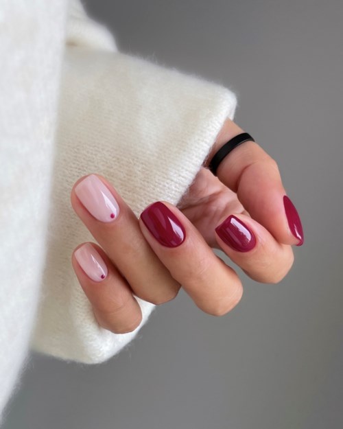 A hand with painted nails, some nails are pink and others are dark red, wearing a black ring and white sweater.