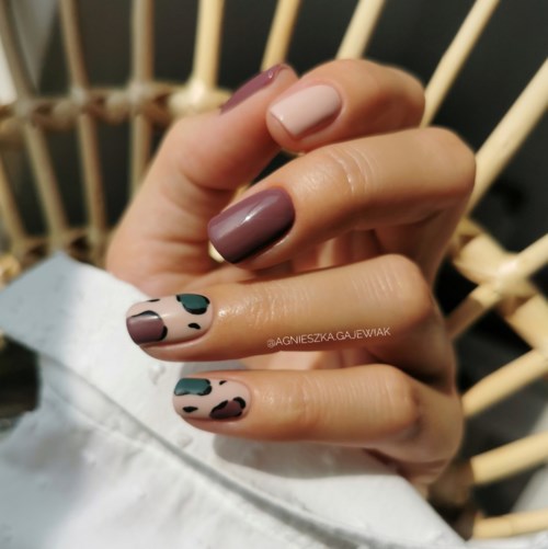 Nails painted with different shades and patterns, some plain and others with colorful spots. Hand close-up against a wooden background.