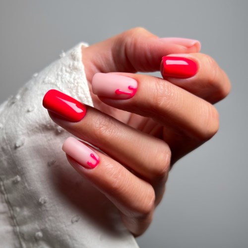 Nail polish on fingers, mostly red with pink accents, held against light grey background.