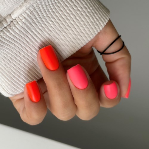 En hand visar nagellack i ljus orange och rosa, med en beige stickad ärm och en svart ring.