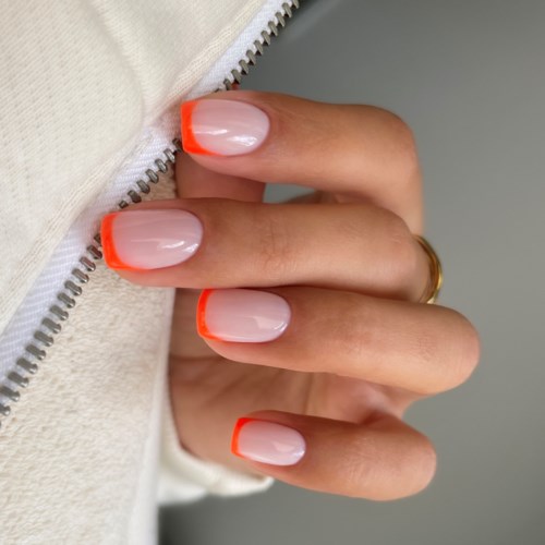 Hand med naglar målade i beige färg och ljus orange tips, håller i ett blixtlås. Enkel och färgglad design.