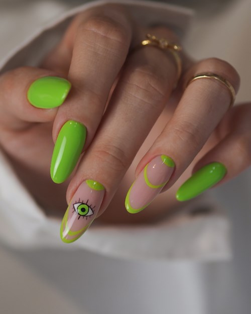Nail art med ljusgrön nagellack, ett design med öga och ögonfransar på en nagel, och en gul accent på andra.