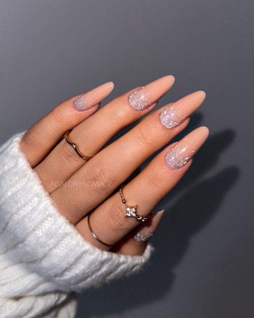 Hand with decorated nails, wearing rings, partly covered by a white sweater sleeve.