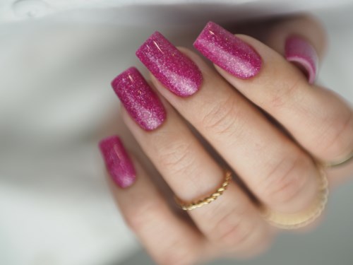 Närbild på en hand med långa rosa glittriga naglar och rings på fingrarna.