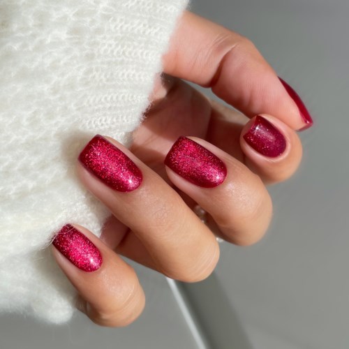 Hand mit roten, glitzernden Nägeln, die weißen Stoff hält.