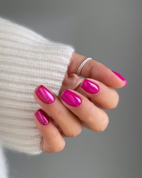 A hand with bright pink nails and a silver ring, partly covered by a white knitted sleeve.