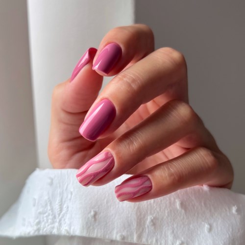 Nails painted pink with white marbled patterns, held near a white cloth and bright light.